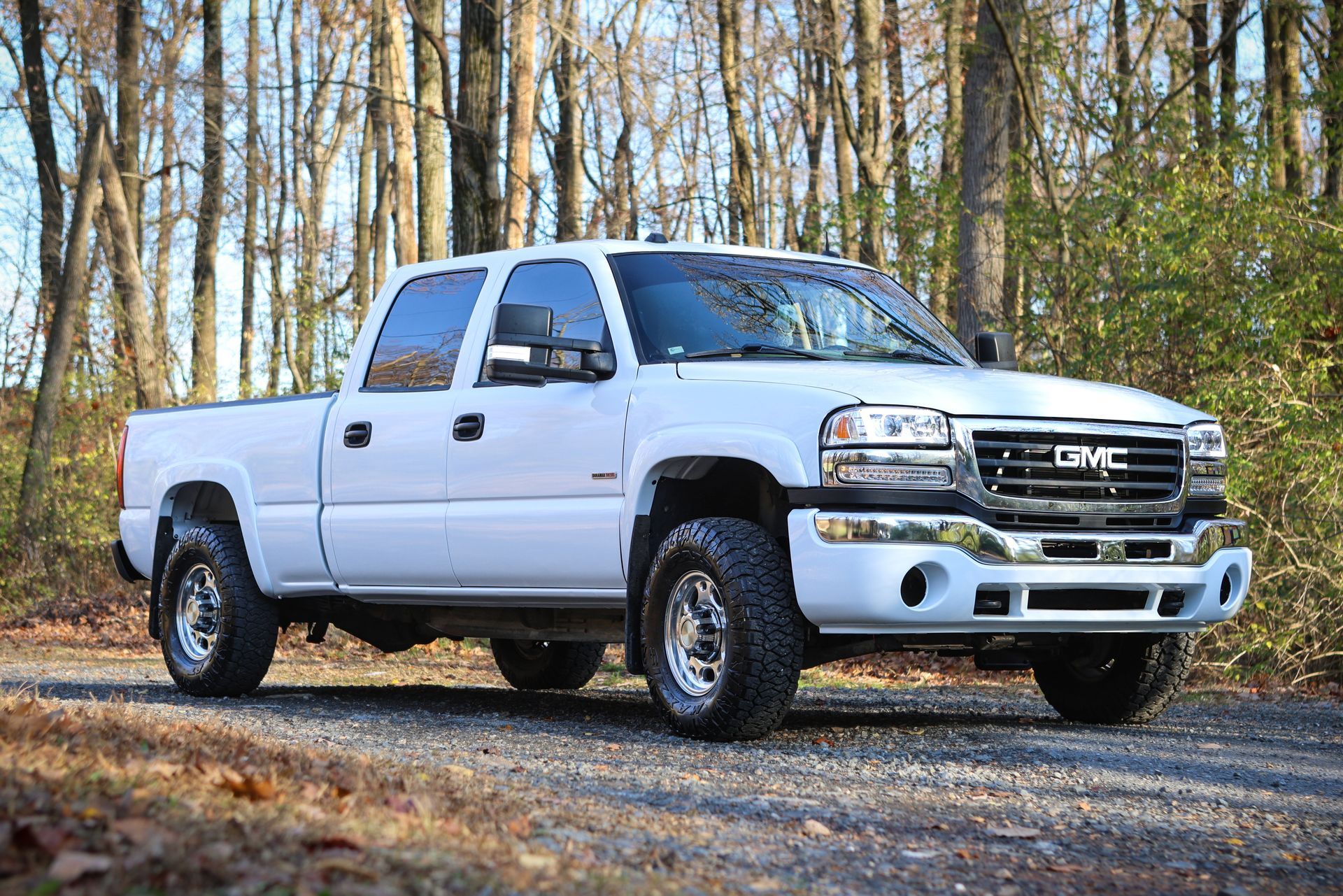 White GMC pickup truck parked on a gravel road surrounded by trees.