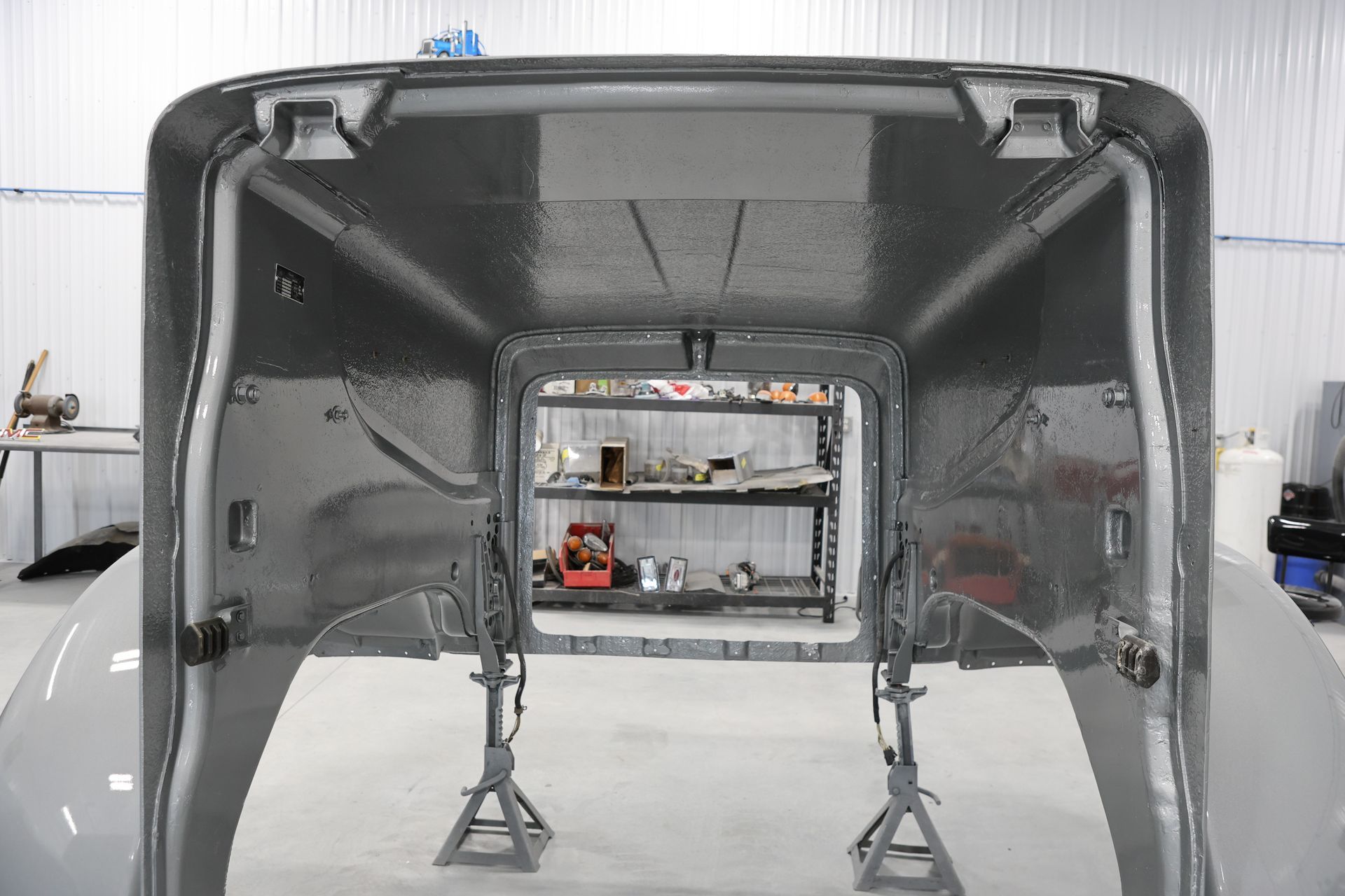 Inside of a vehicle hood, painted gray, supported by jack stands in a workshop.