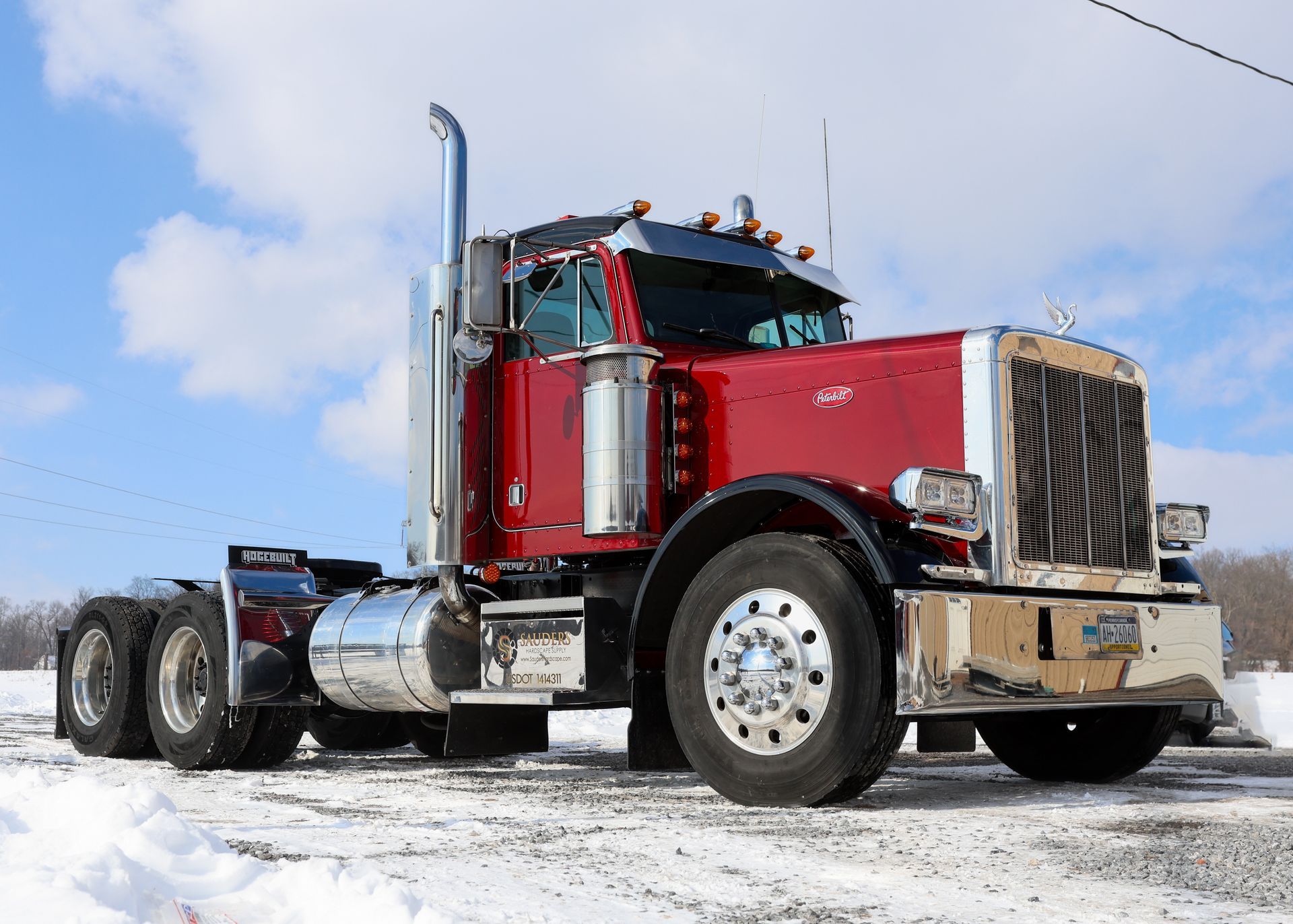 Red and chrome semi-truck in snowy setting, parked with sunlit, blue sky.