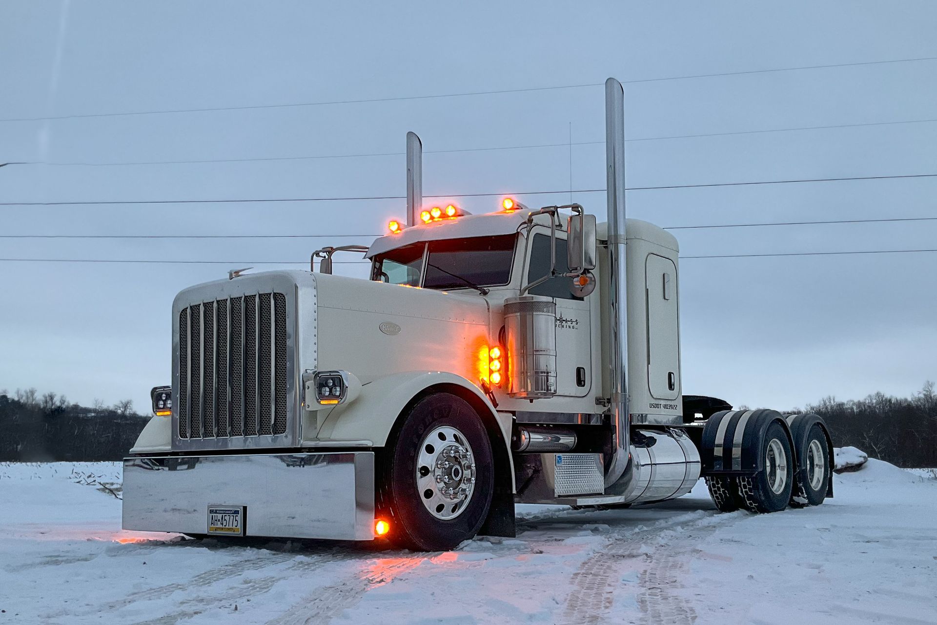 White semi-truck in snowy setting; running lights on.