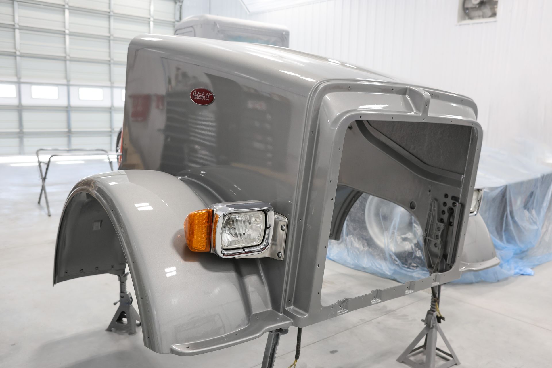A gray Peterbilt truck cab undergoing paintwork in a white workshop.