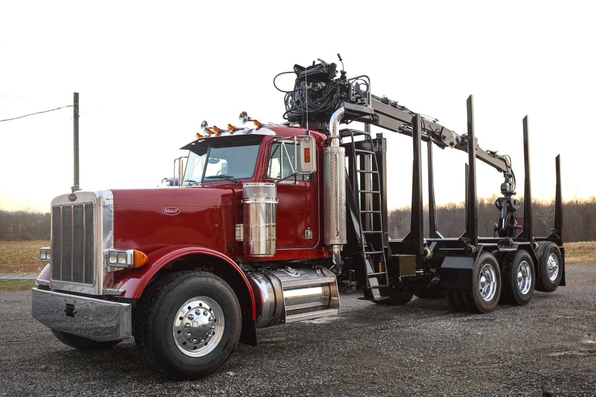 Red logging truck with crane and trailer, parked outside on a cloudy day.