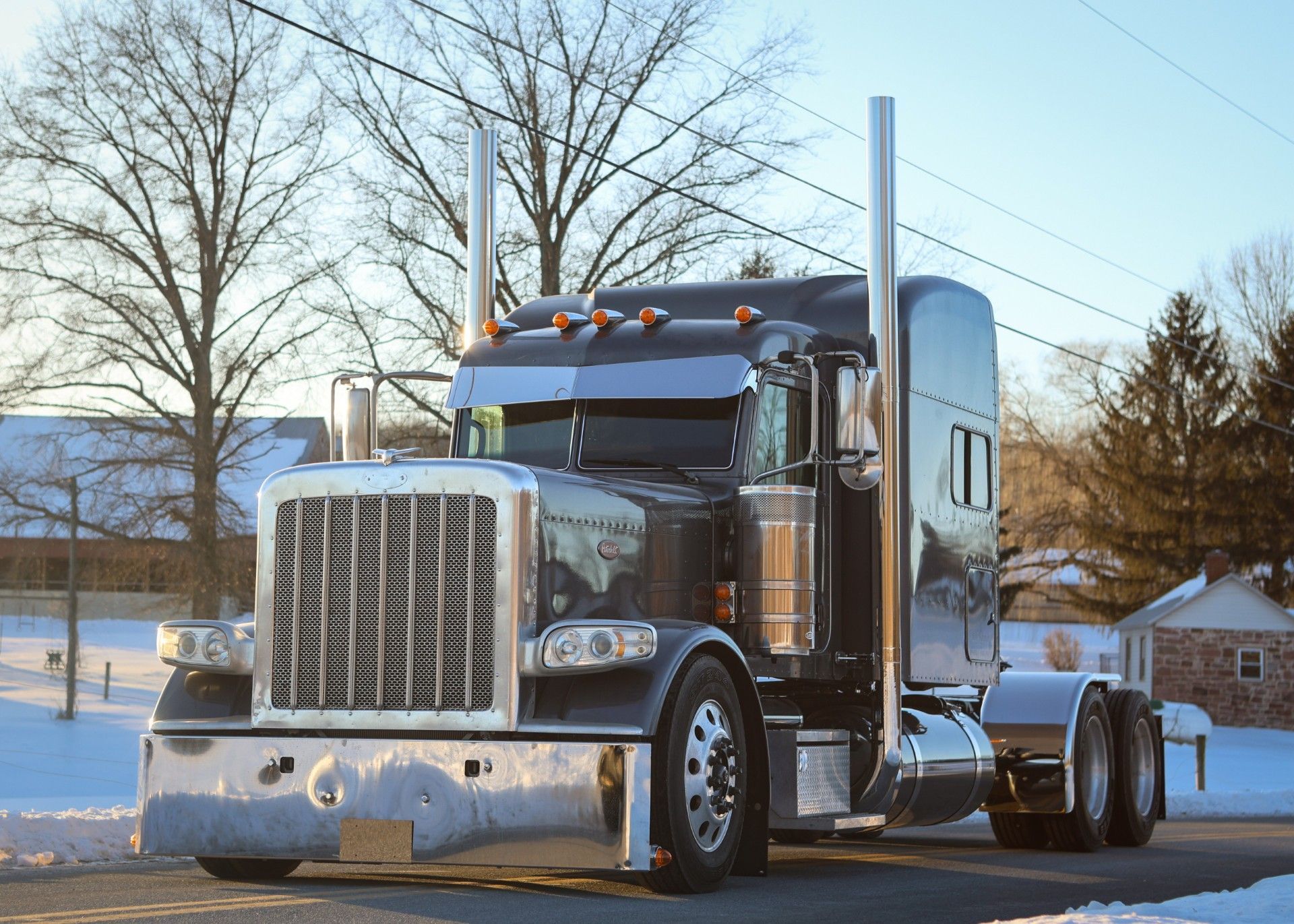 Shiny black semi-truck parked on a road, front end in view. Chrome details, tall exhaust stacks, snowy background.