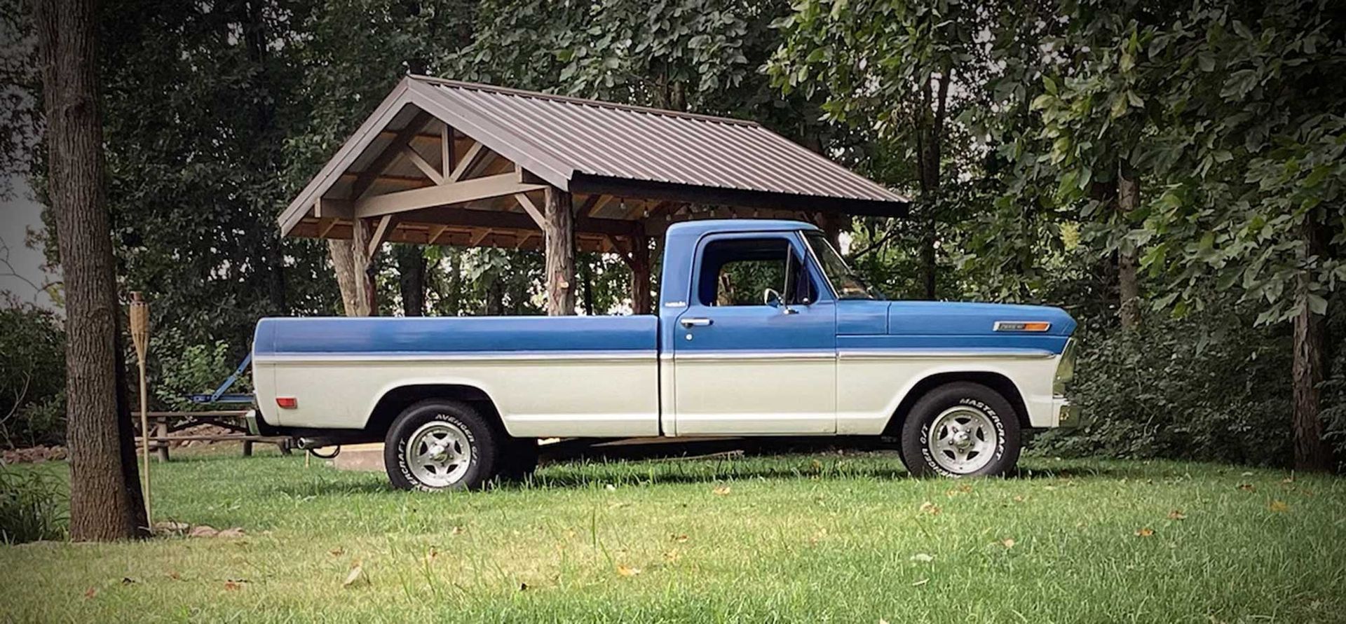 A blue and white truck is parked in the grass under a gazebo