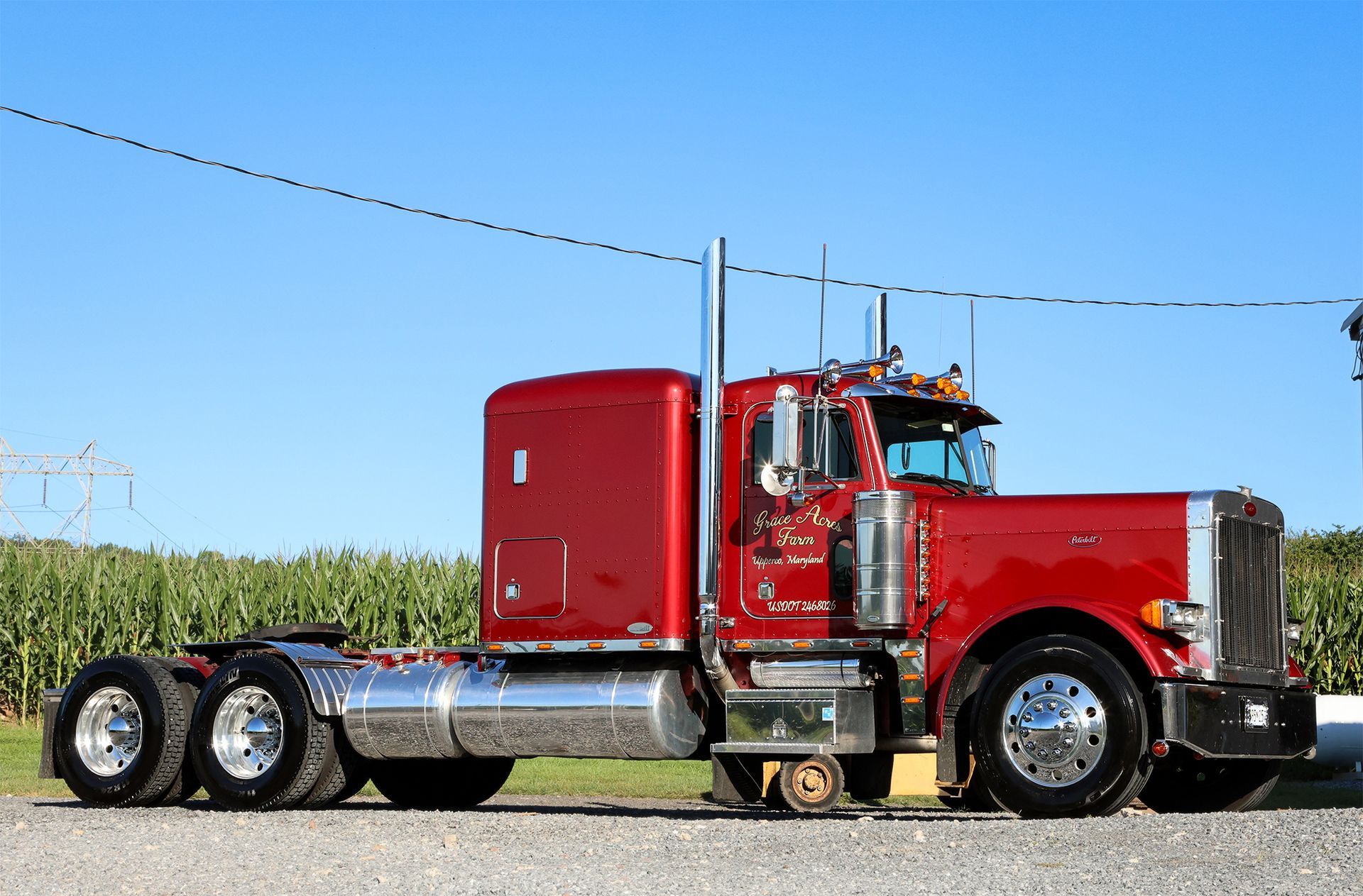 Red Peterbilt semi-truck parked on gravel, chrome details, blue sky background.