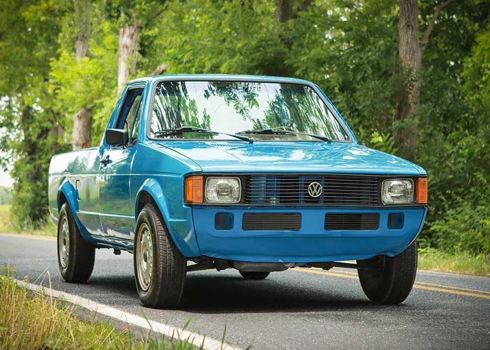 A blue volkswagen caddy pickup truck is driving down a country road
