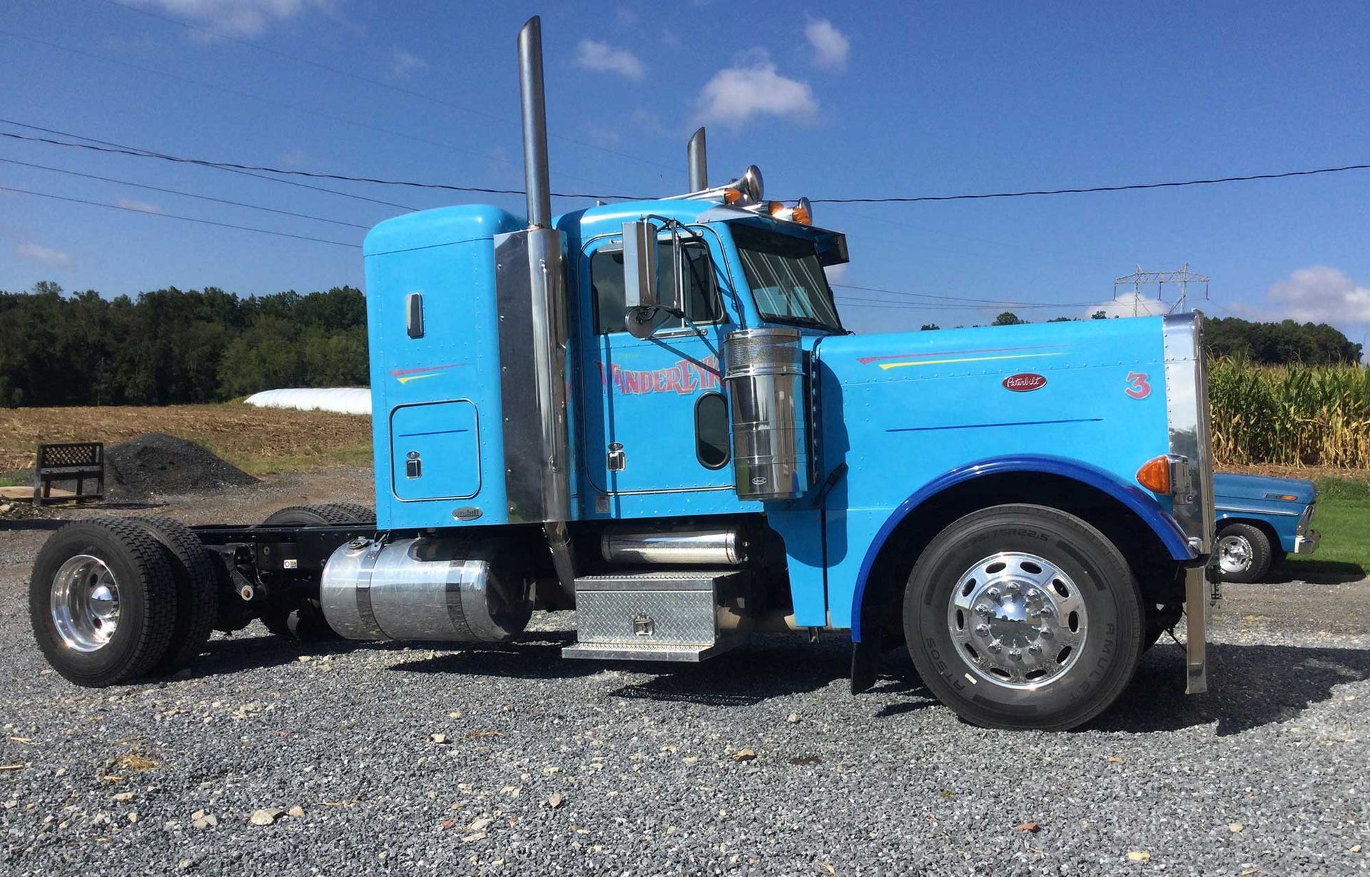 A blue semi truck is parked in a gravel lot