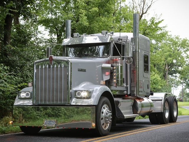A light silver semi truck is driving down a highway.