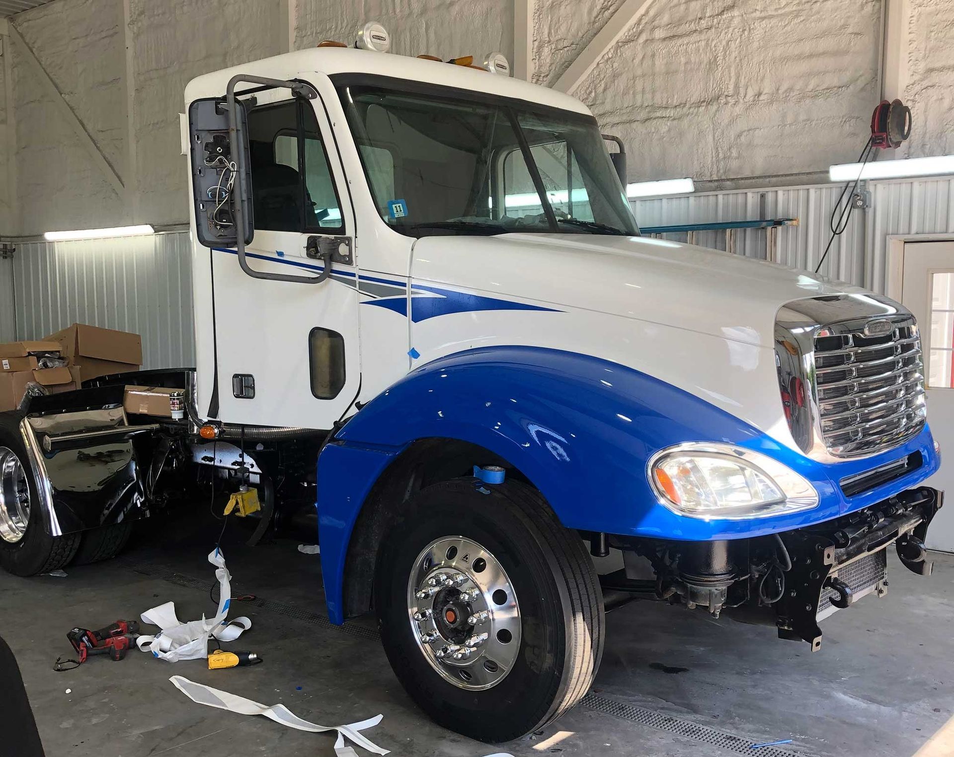 A white truck with blue fenders is parked in a garage