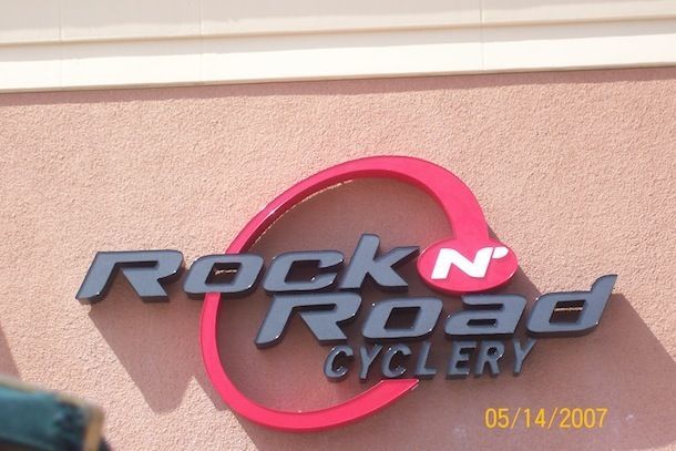 A rock n road cyclery sign on a pink wall