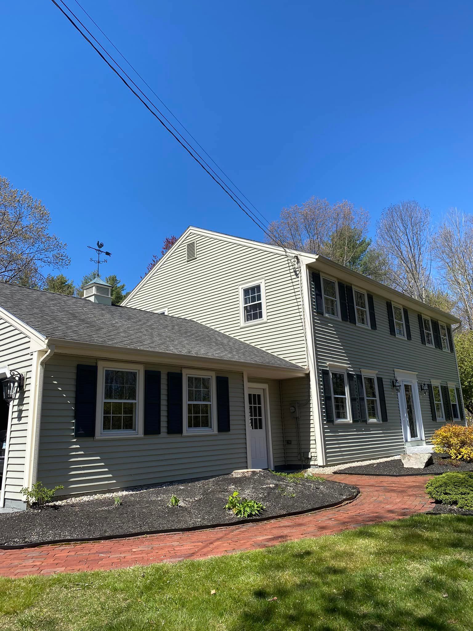 Two-story house with green siding, black shutters, white trim, and red brick walkway on a sunny day.