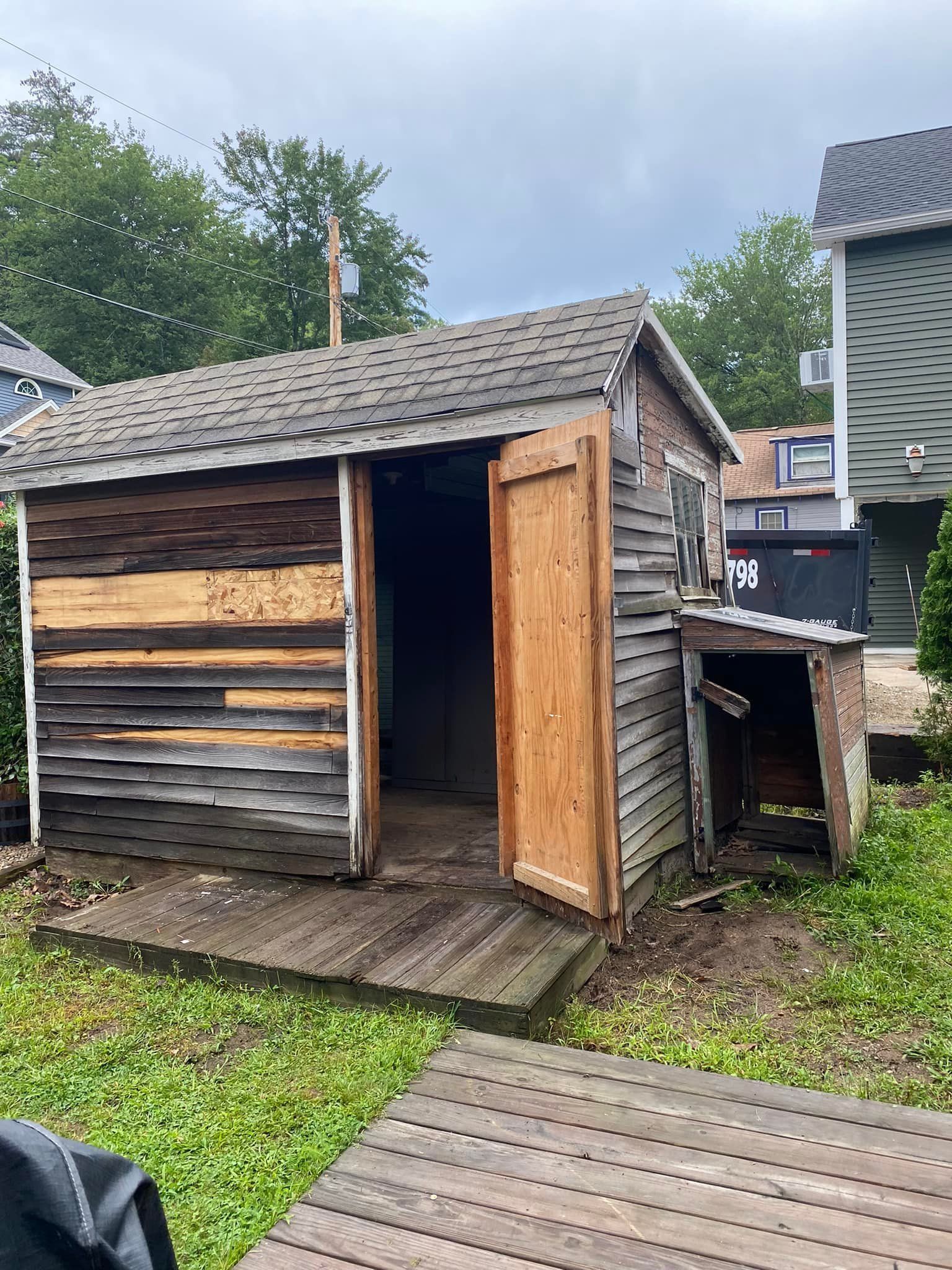 Weathered wooden shed with open door on a grassy yard.