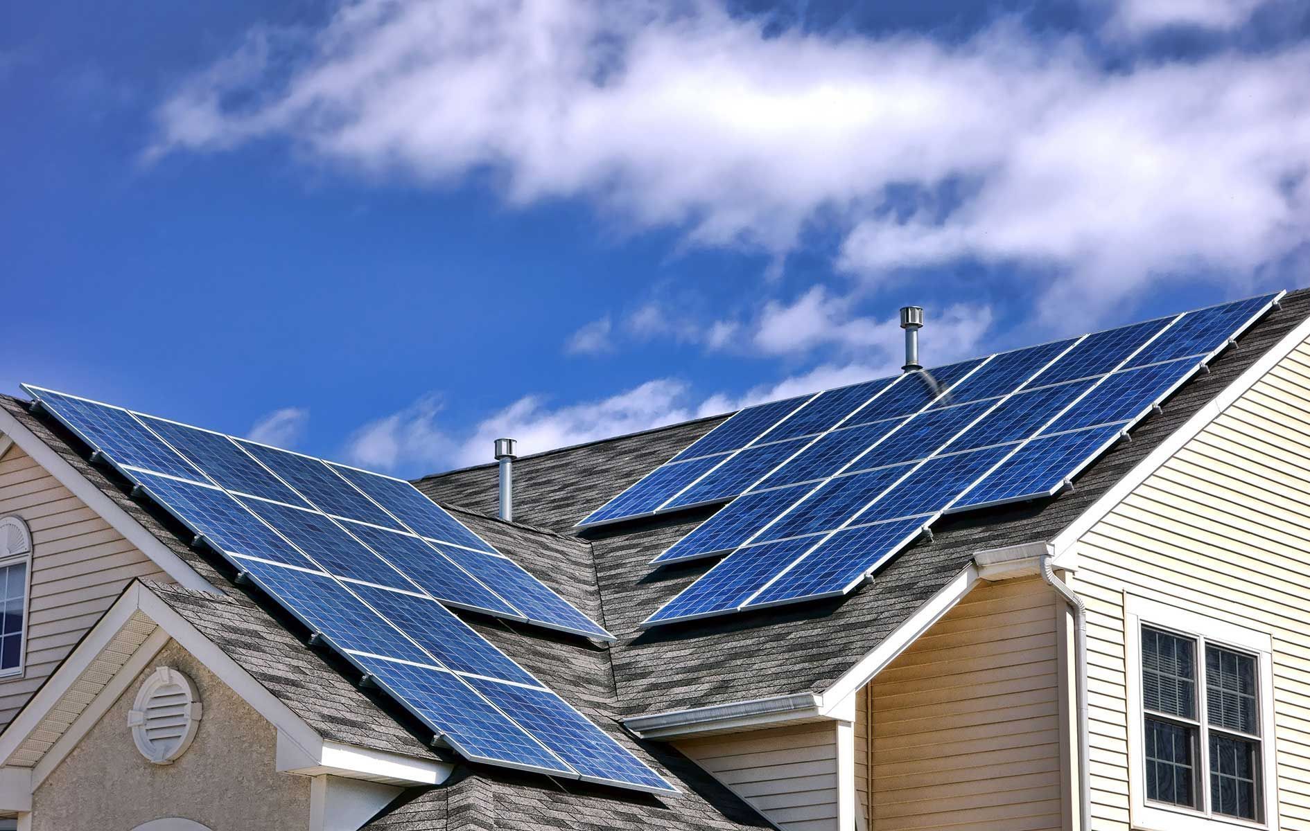 Solar panels installed on a residential roof, capturing sunlight, against a blue sky.