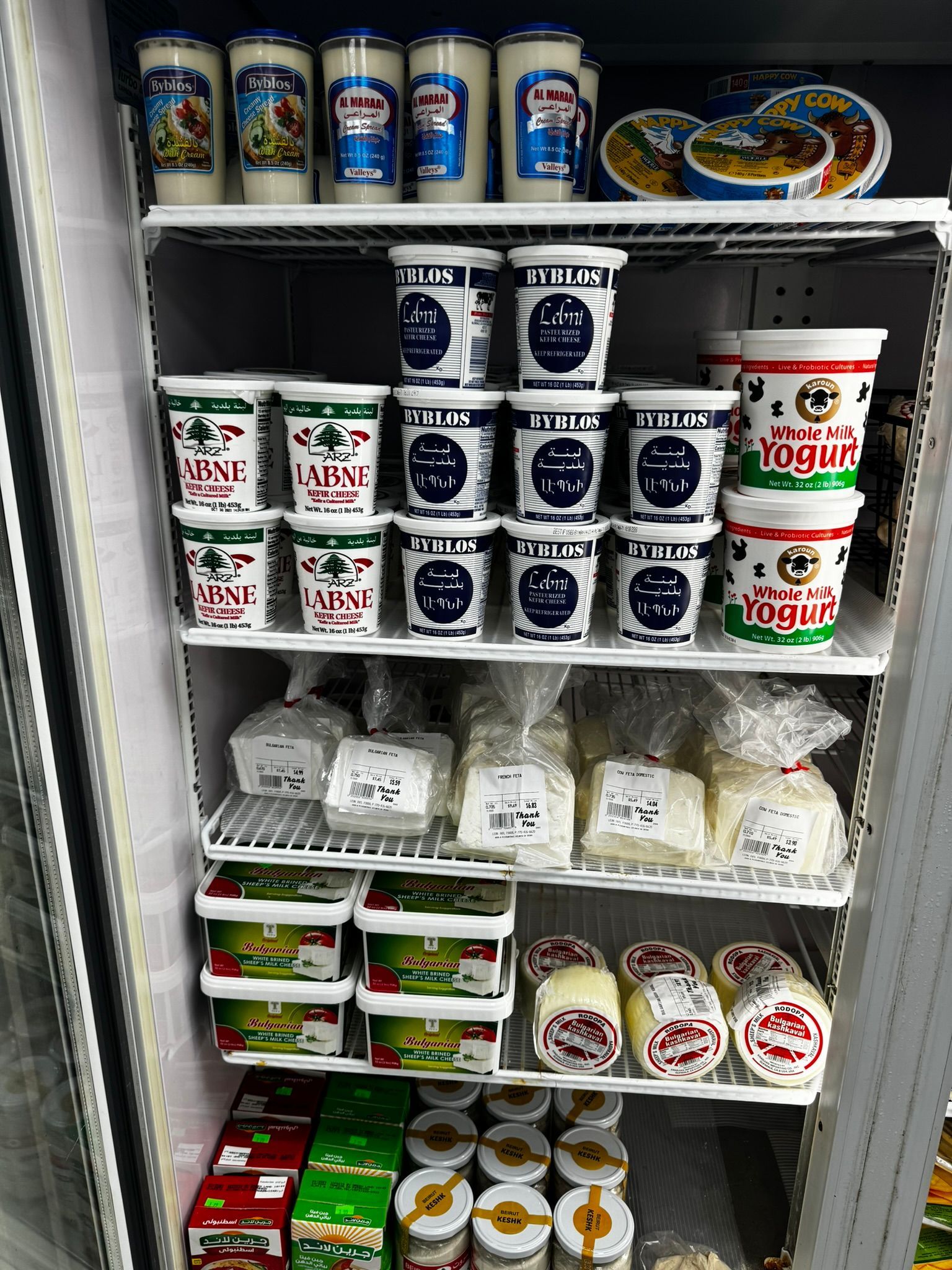 Refrigerated display stocked with assorted dairy cups, yogurt tubs, and snack containers on white shelves