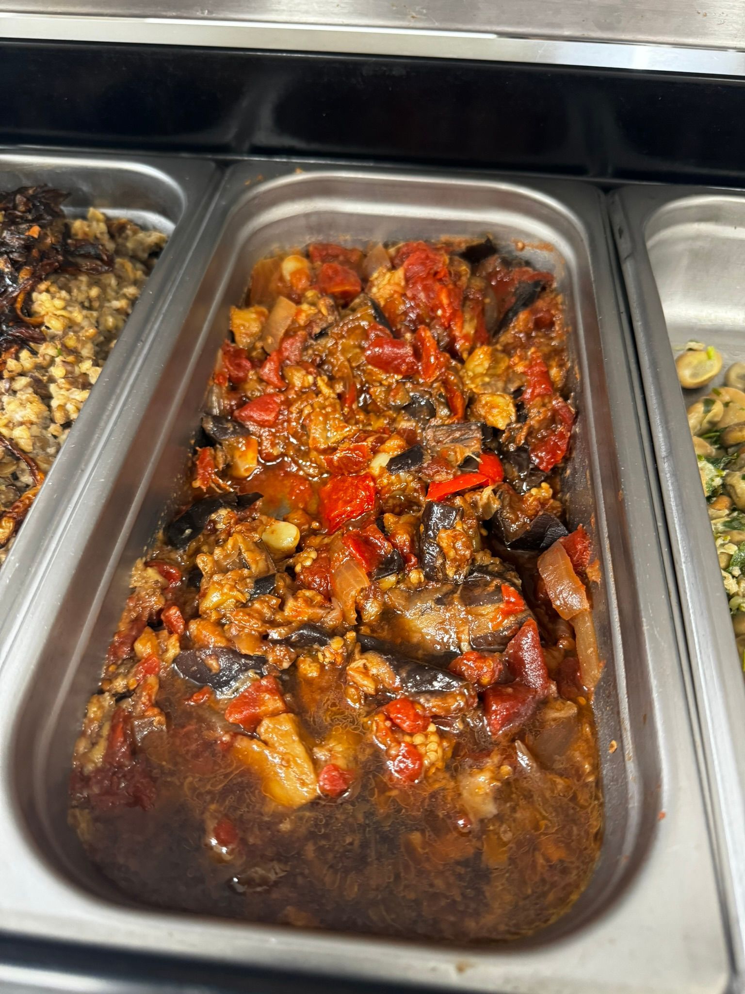 Tray of roasted mixed vegetables in a buffet pan, coated in a dark sauce.