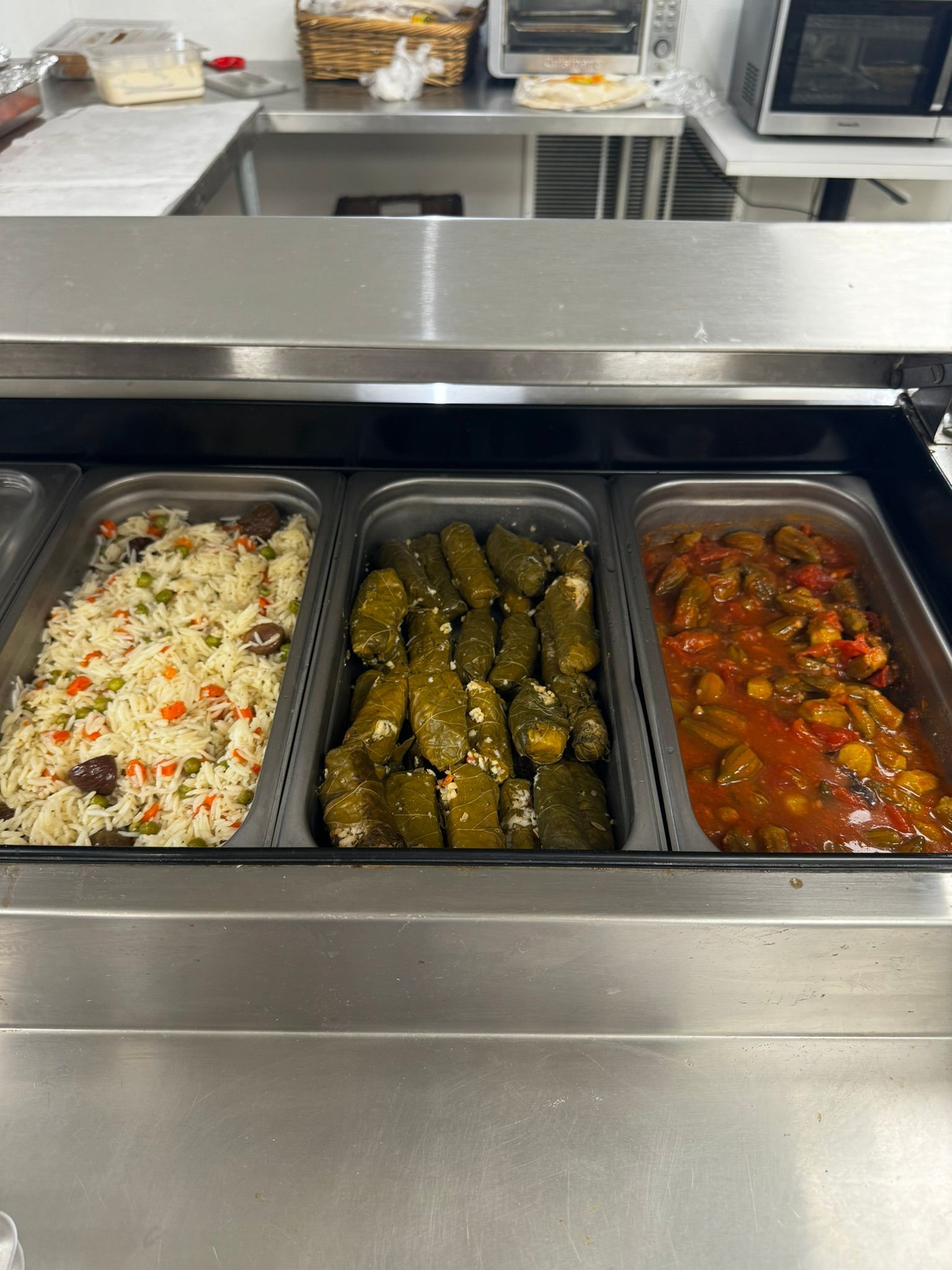 Buffet steam table with three pans of rice, stuffed grape leaves, and tomato vegetable stew