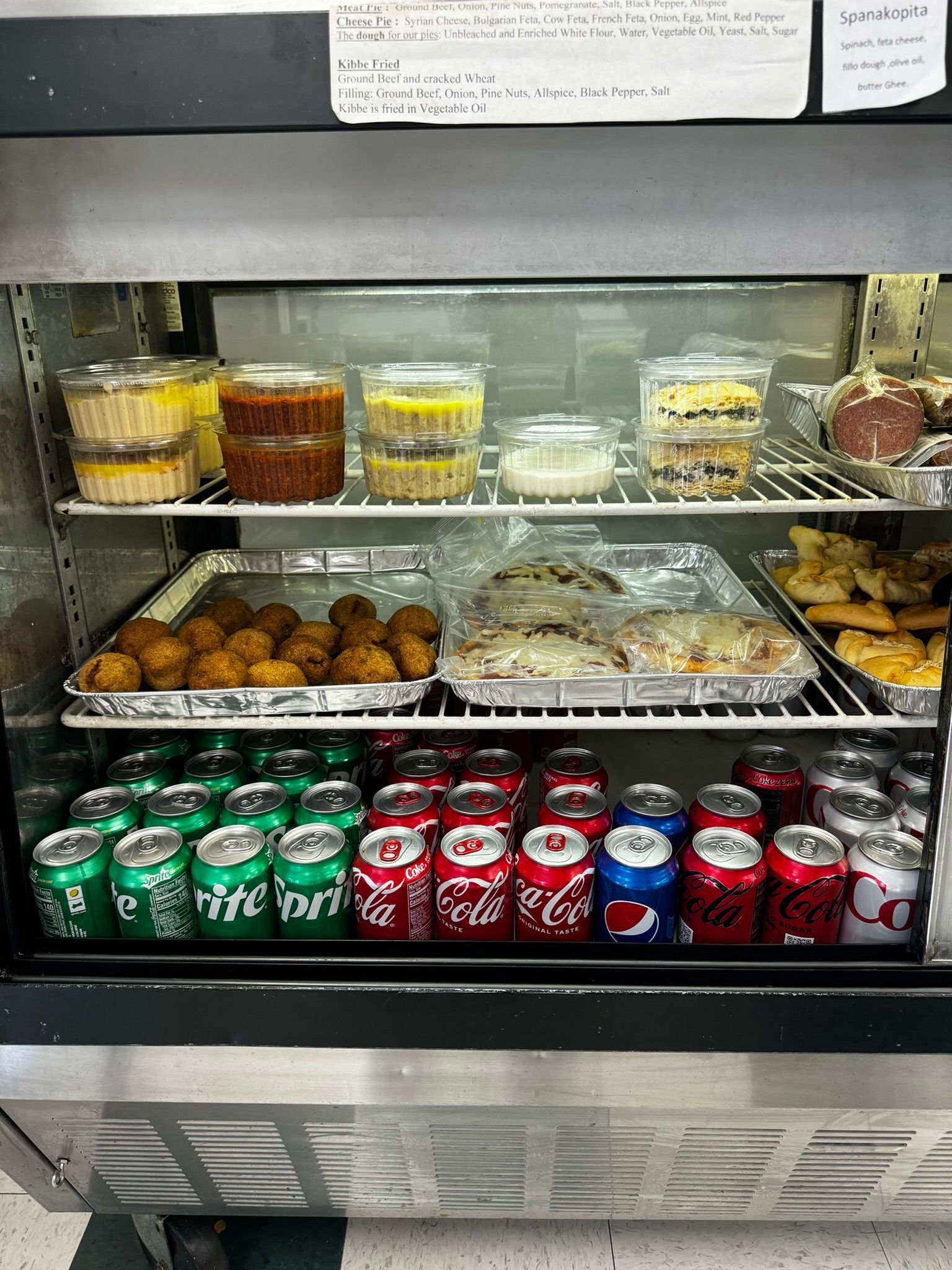 Refrigerated display case with desserts, snacks, and cans of soda arranged on shelves