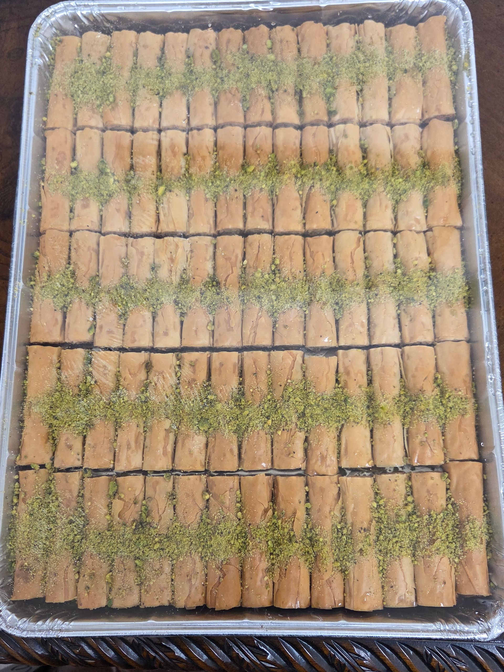 Tray of rolled wafer cookies dusted with powdered sugar and cinnamon in a foil pan
