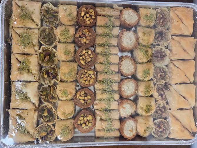 Tray of assorted Middle Eastern pastries arranged in neat rows, including baklava and rolled sweets.