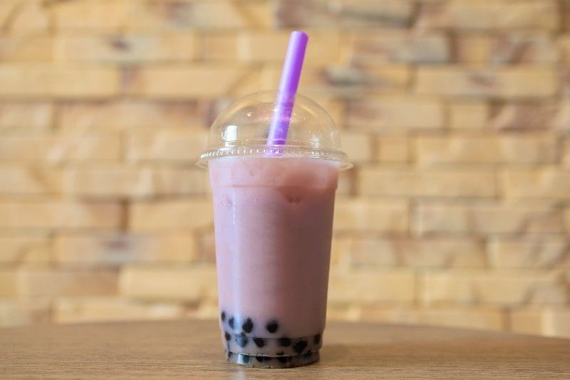 A purple bubble tea with a purple straw in a plastic cup on a table.