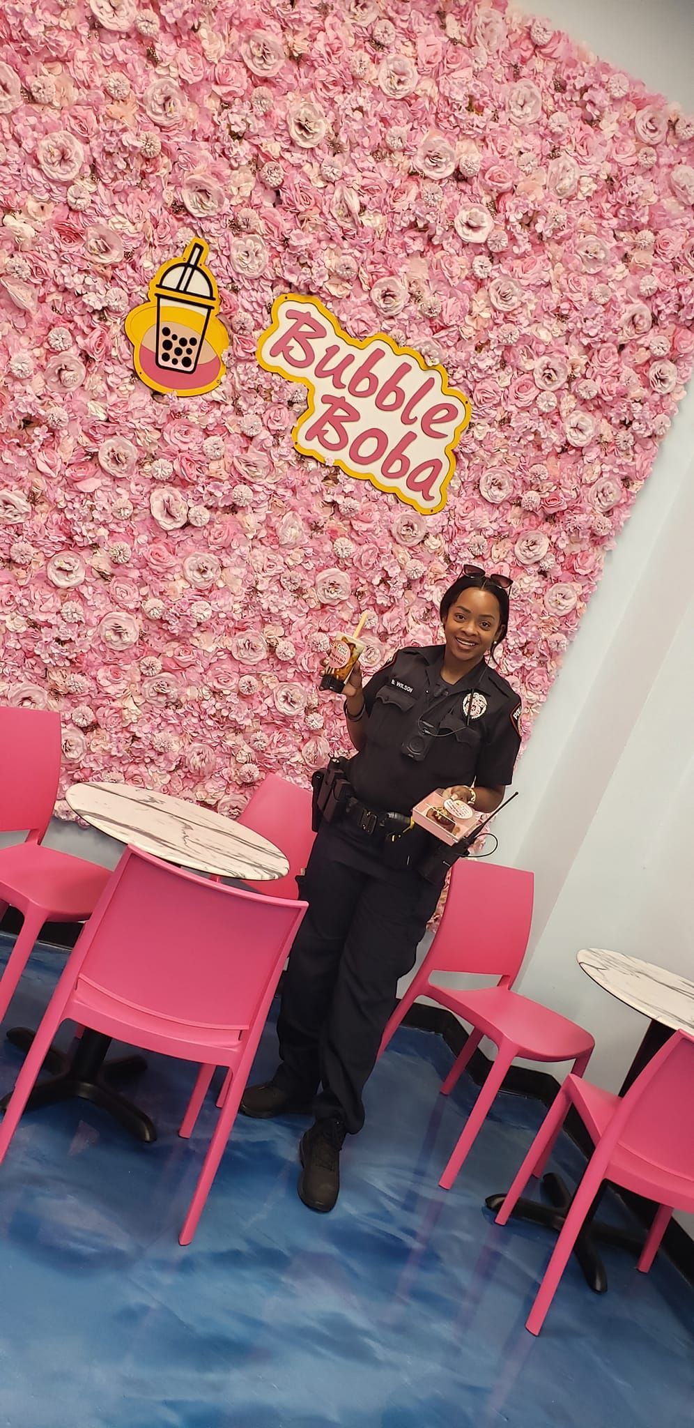 A police officer is standing in front of a wall of pink flowers in a restaurant.