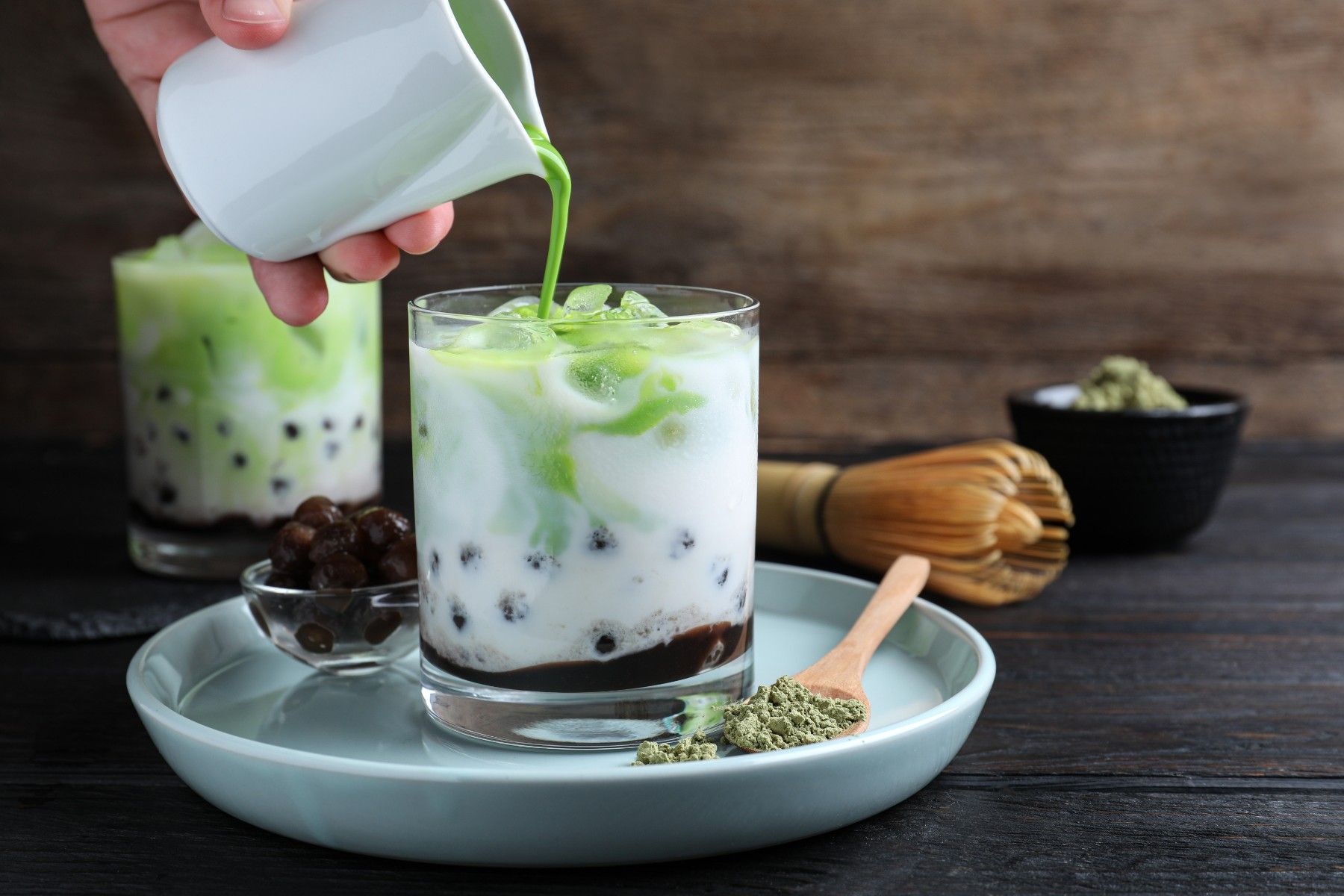 A person is pouring green tea into a glass of milk.