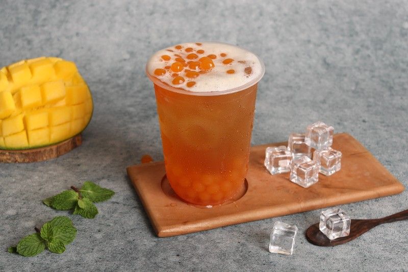 A cup of tea is sitting on a wooden tray next to ice cubes and a mango.