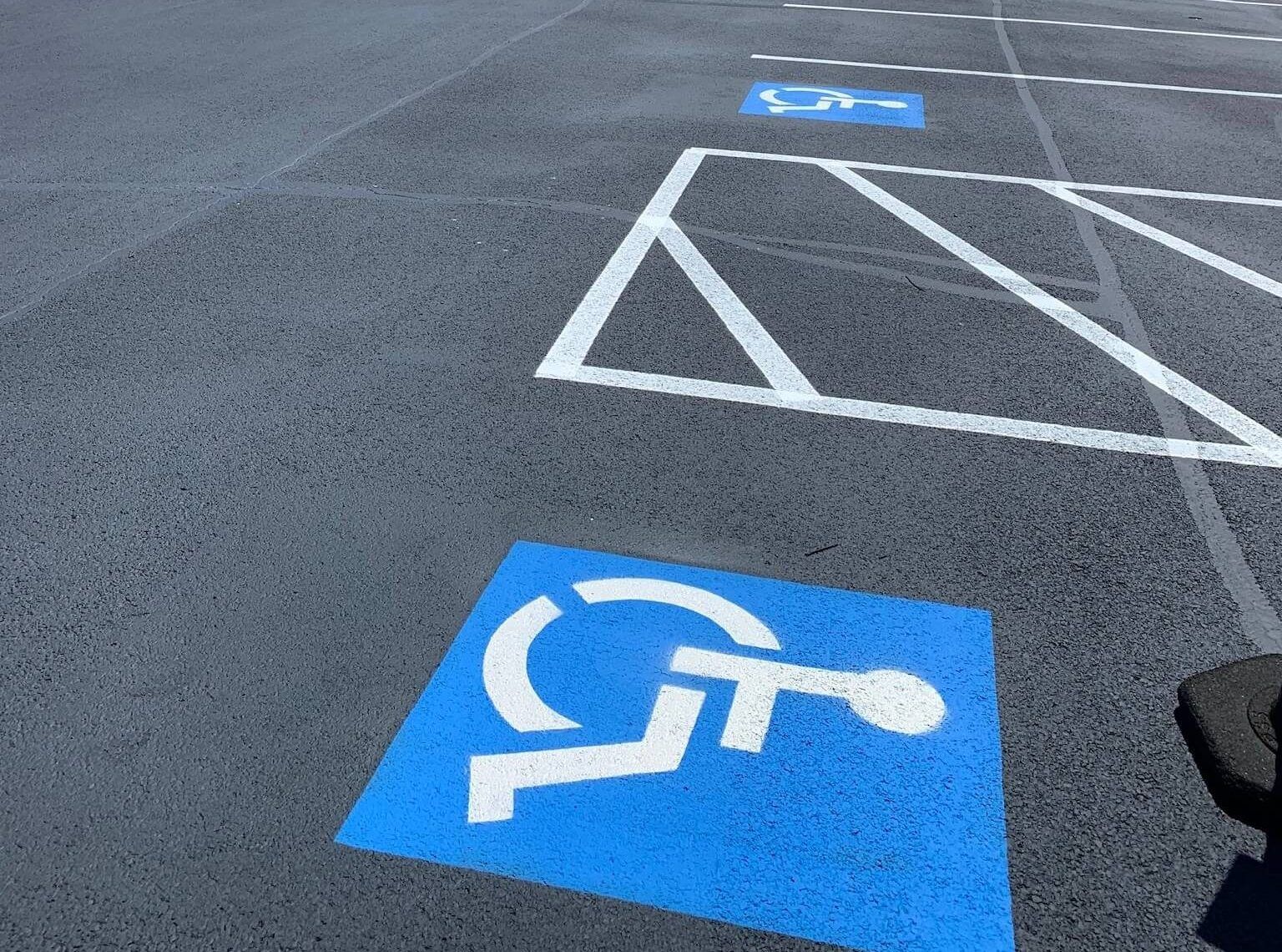 A blue handicapped sign is painted on the ground in a parking lot.