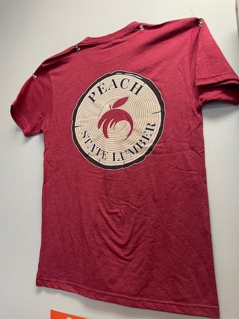 A peach state lumber t-shirt is hanging on a wall