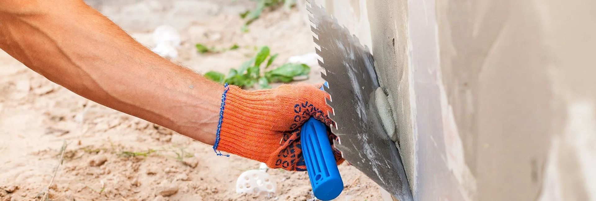 A person wearing an orange glove using a saw on a wall outside.