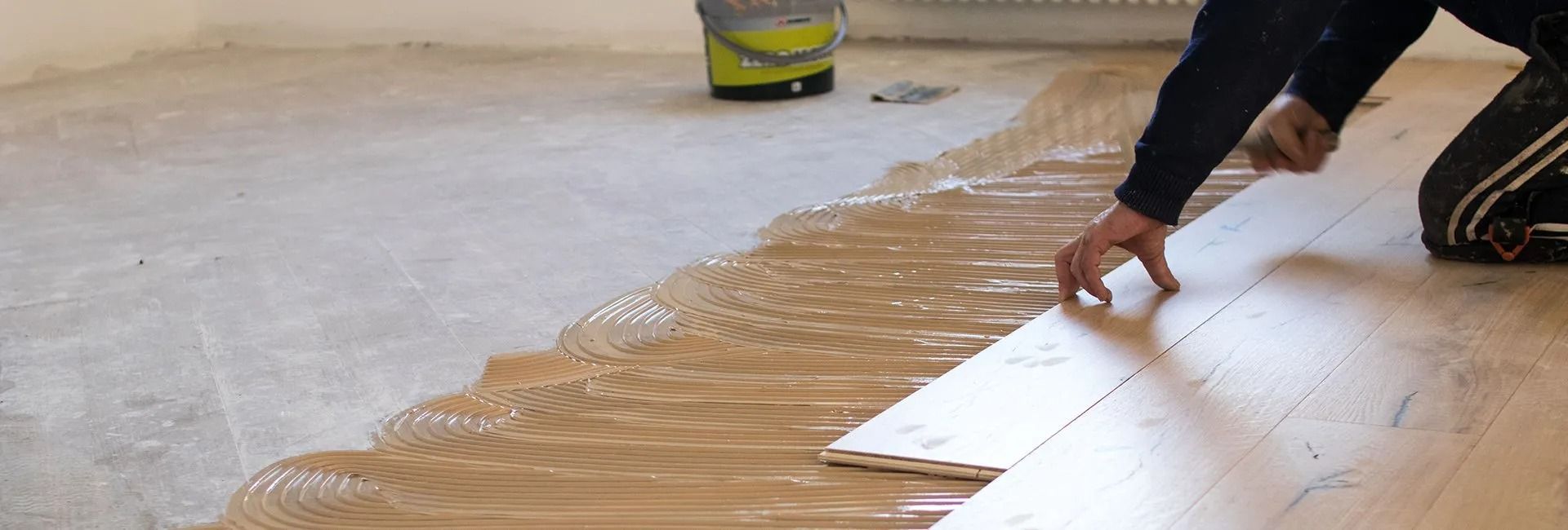 Person laying wooden flooring with glue on a concrete surface.