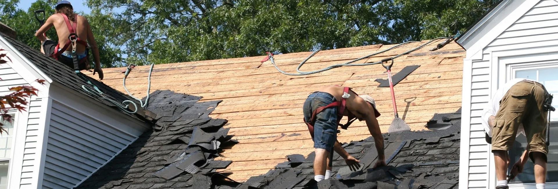Roofers removing old shingles from a house roof on a sunny day.