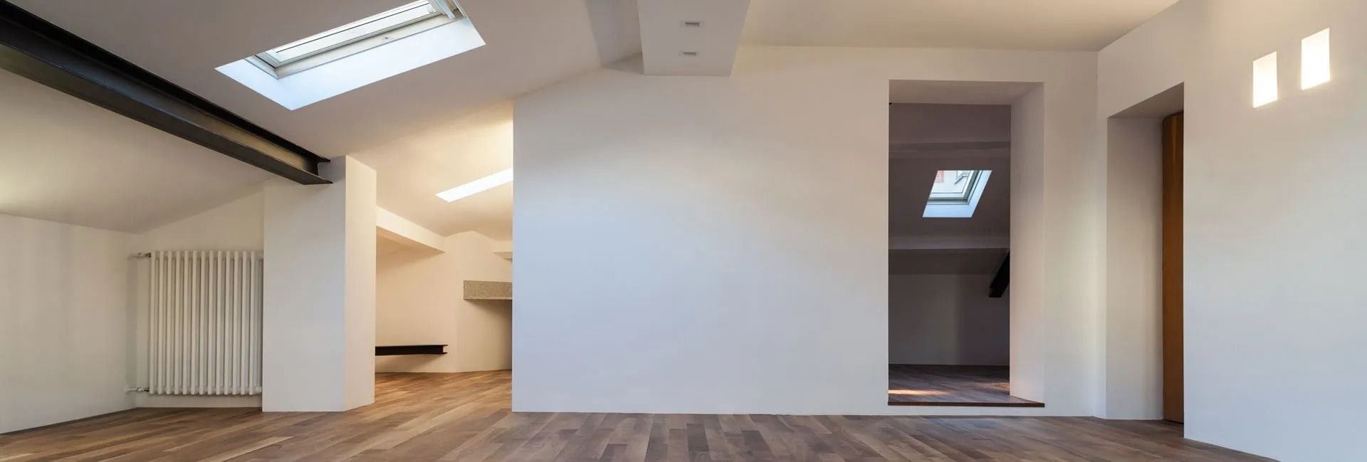 Interior view of a modern, empty room with wooden floors, white walls, and a skylight.