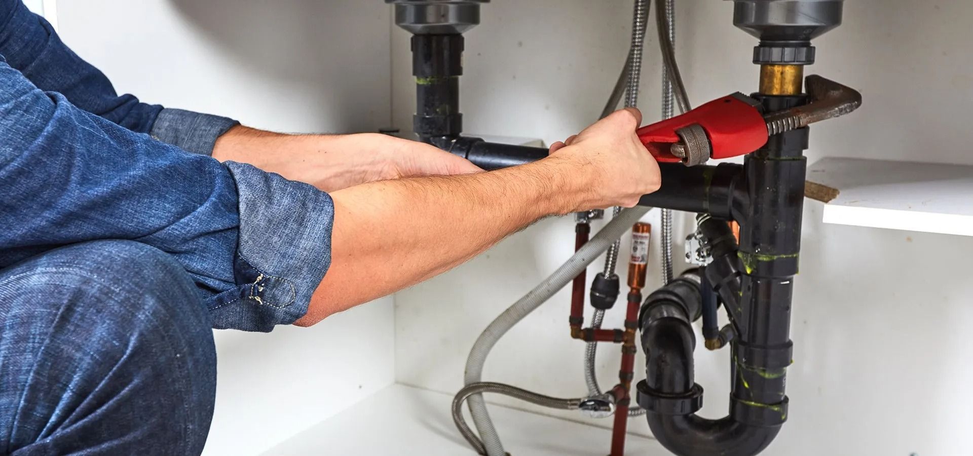 A person is fixing a sink drain with a wrench.