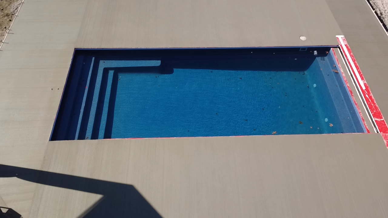 Rectangular blue swimming pool with steps, surrounded by gray concrete.