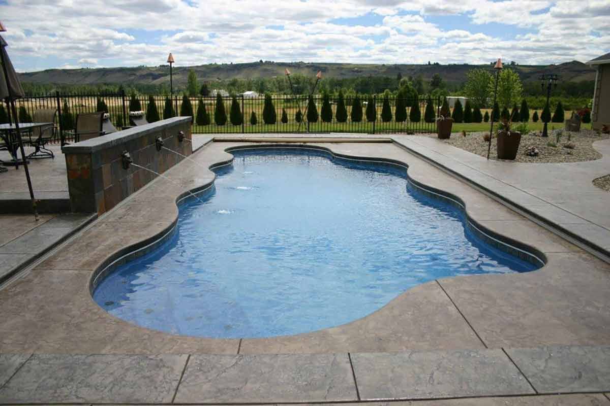 Swimming pool with blue water and stone patio, set against a backdrop of trees and a cloudy sky.