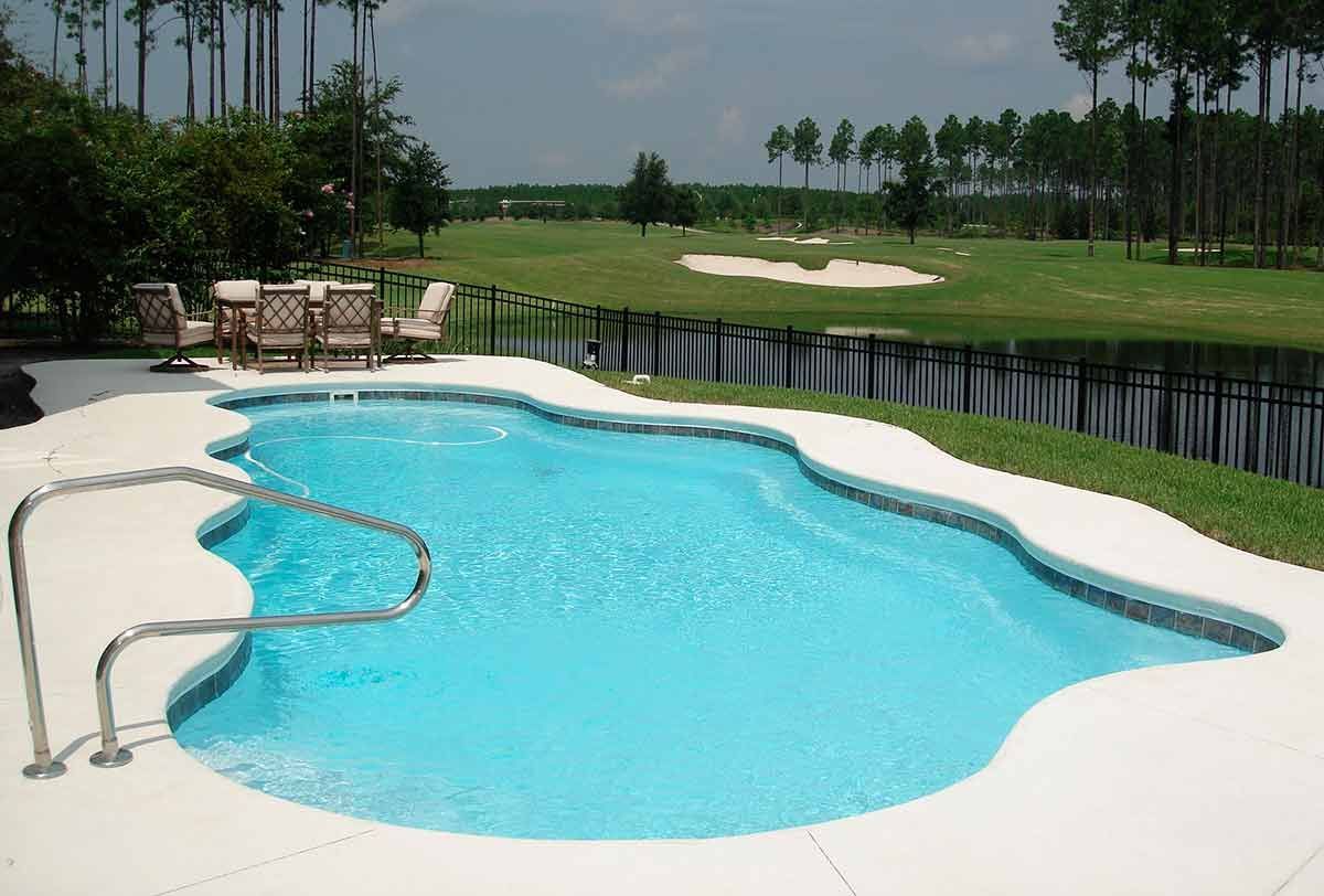 Pool overlooking a golf course. Blue water, white patio, and green grass. Trees in background.