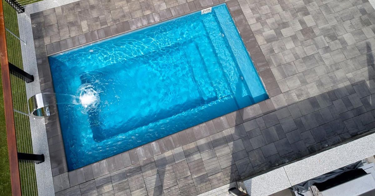 A rectangular in-ground pool with blue water and steps, surrounded by gray paving stones.