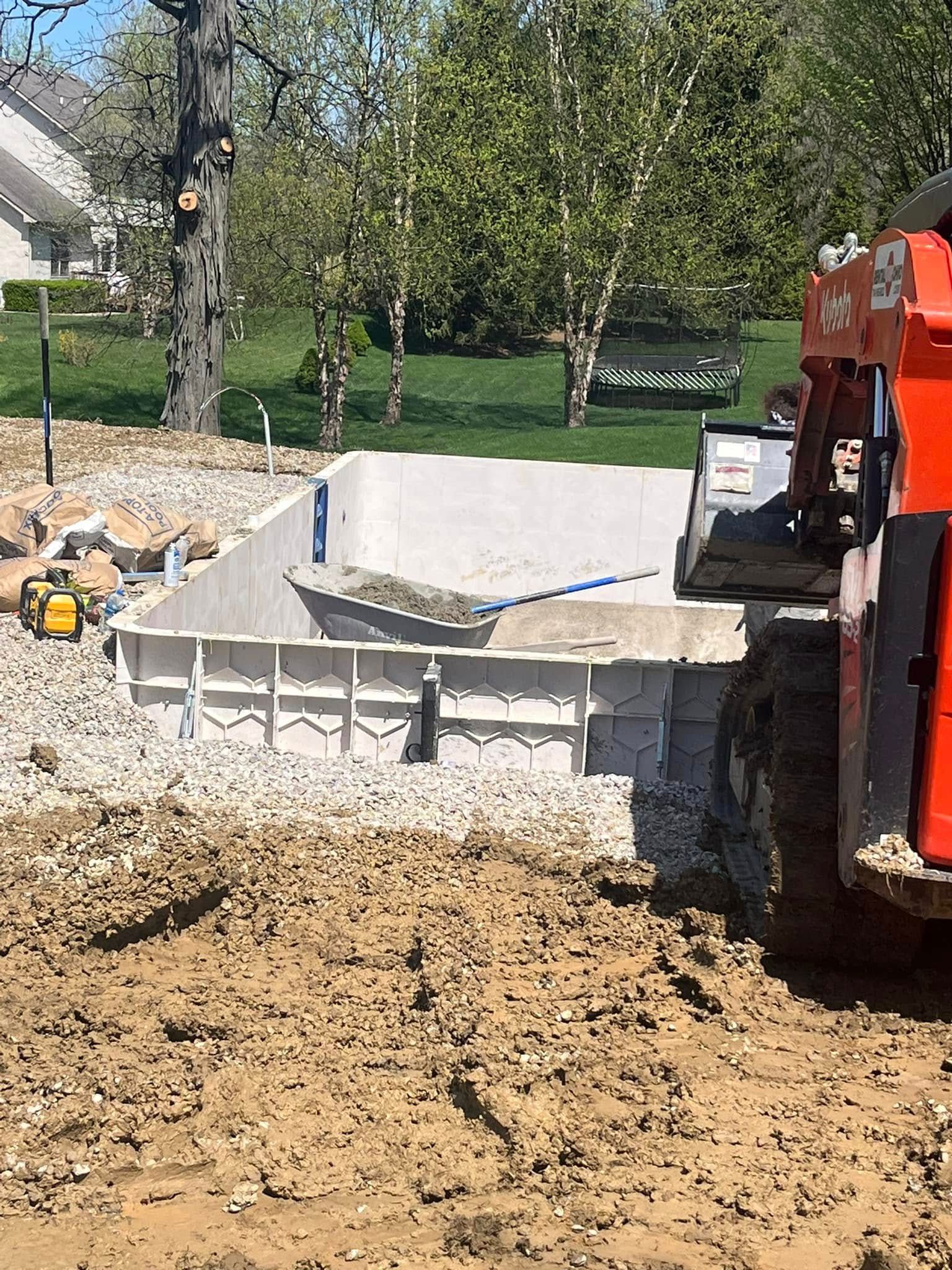 Construction of a concrete pool. A Kubota excavator fills the pool with gravel.
