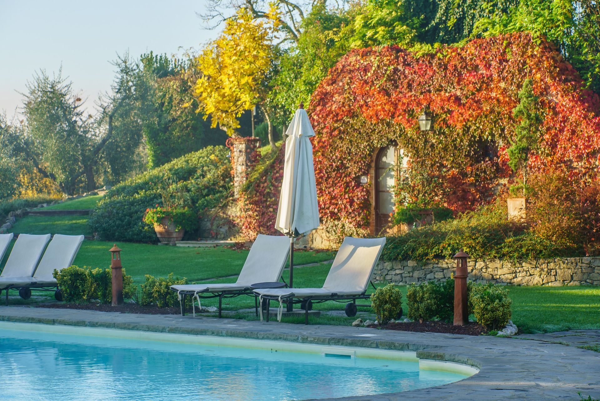 Poolside scene with lounge chairs, closed umbrella, and foliage in autumn colors.