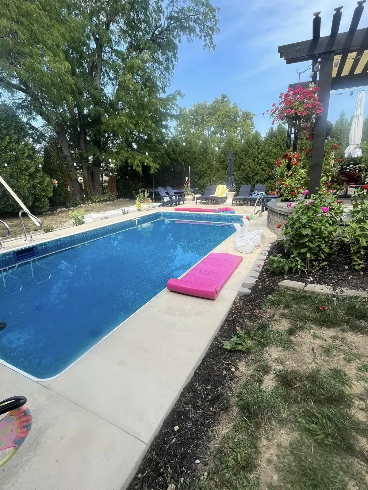 Swimming pool with pink float, surrounded by trees and a pergola.