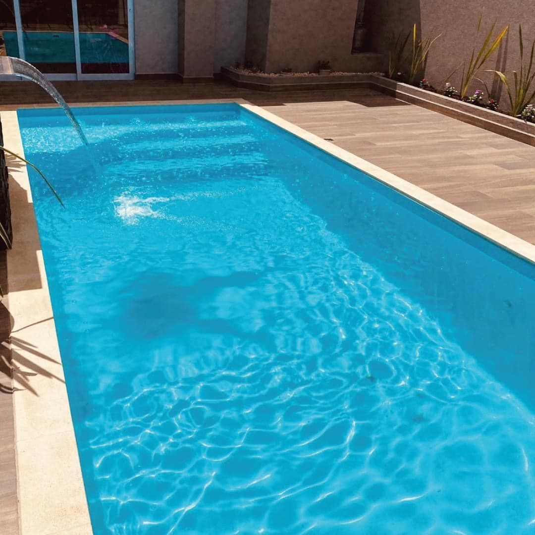 Rectangular swimming pool filled with blue water, with a fountain, on a sunny patio.