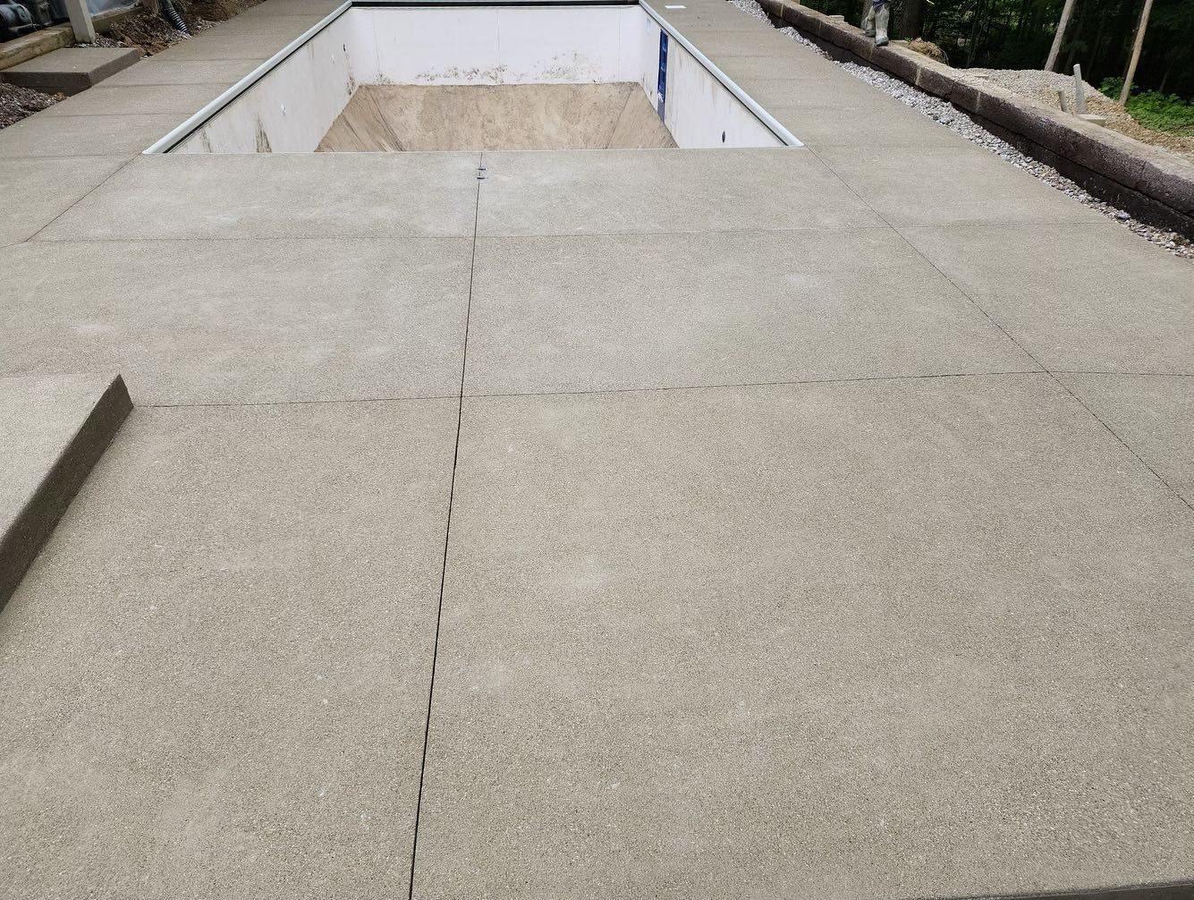 Concrete tiles surrounding an empty pool, outdoors.