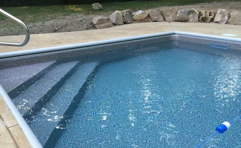 Swimming pool with steps, blue water, and stone coping.