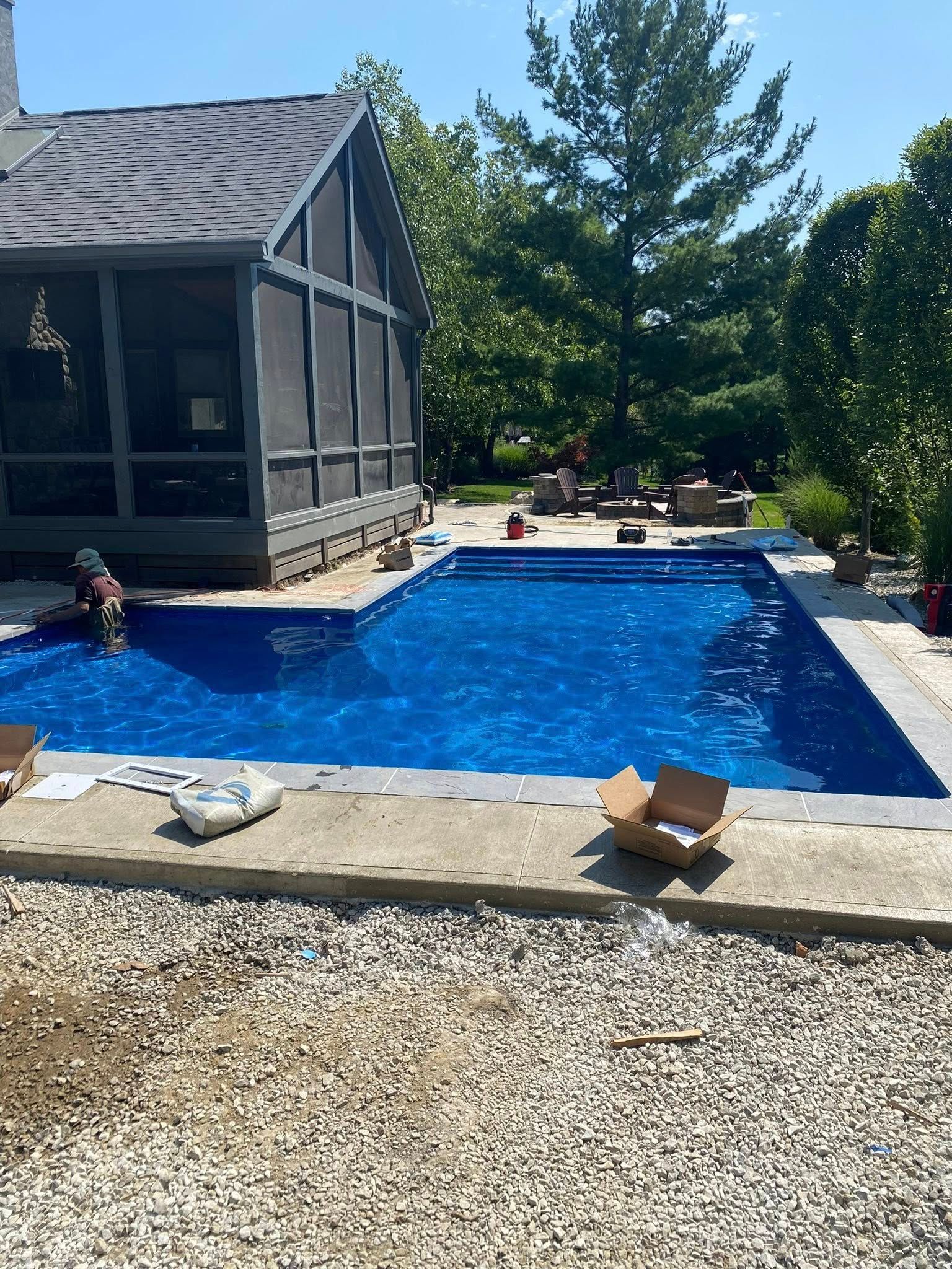 Blue swimming pool with screen porch, surrounded by concrete and gravel.