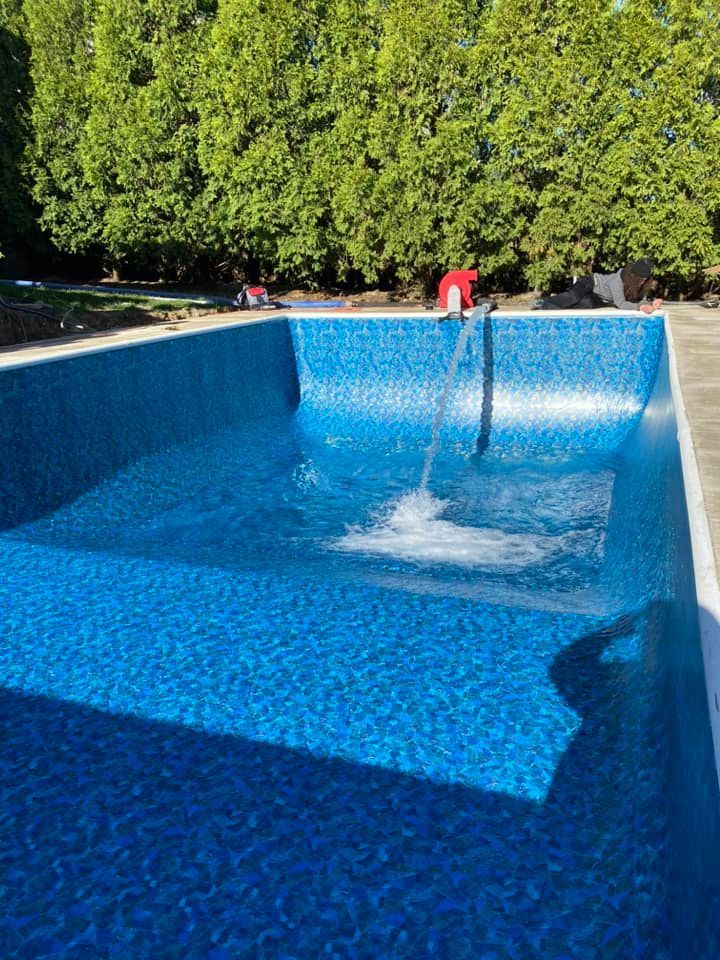 Blue tiled swimming pool filling with water, trees in the background.