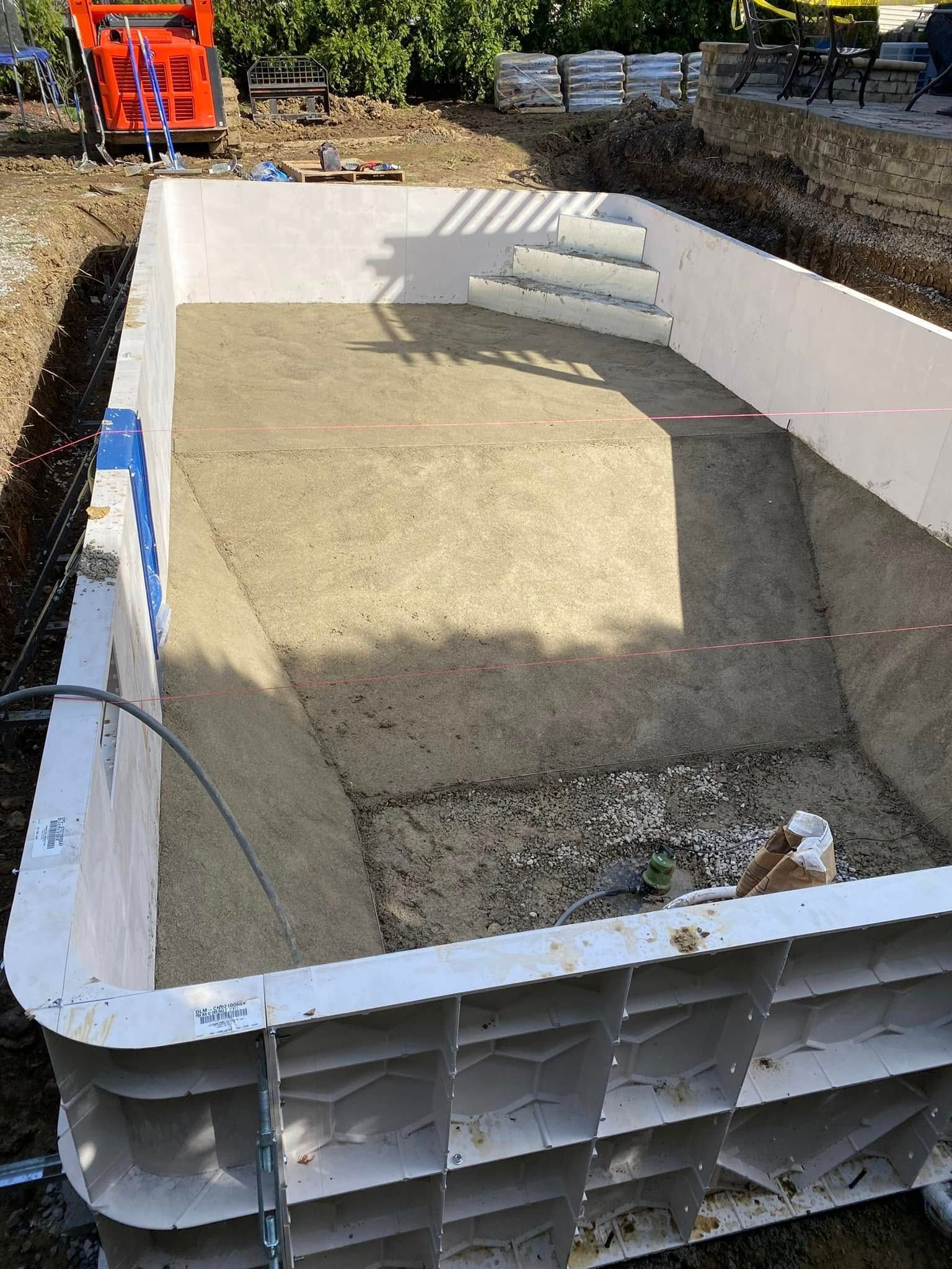 An unfinished rectangular pool structure with steps, cement and gravel in progress.