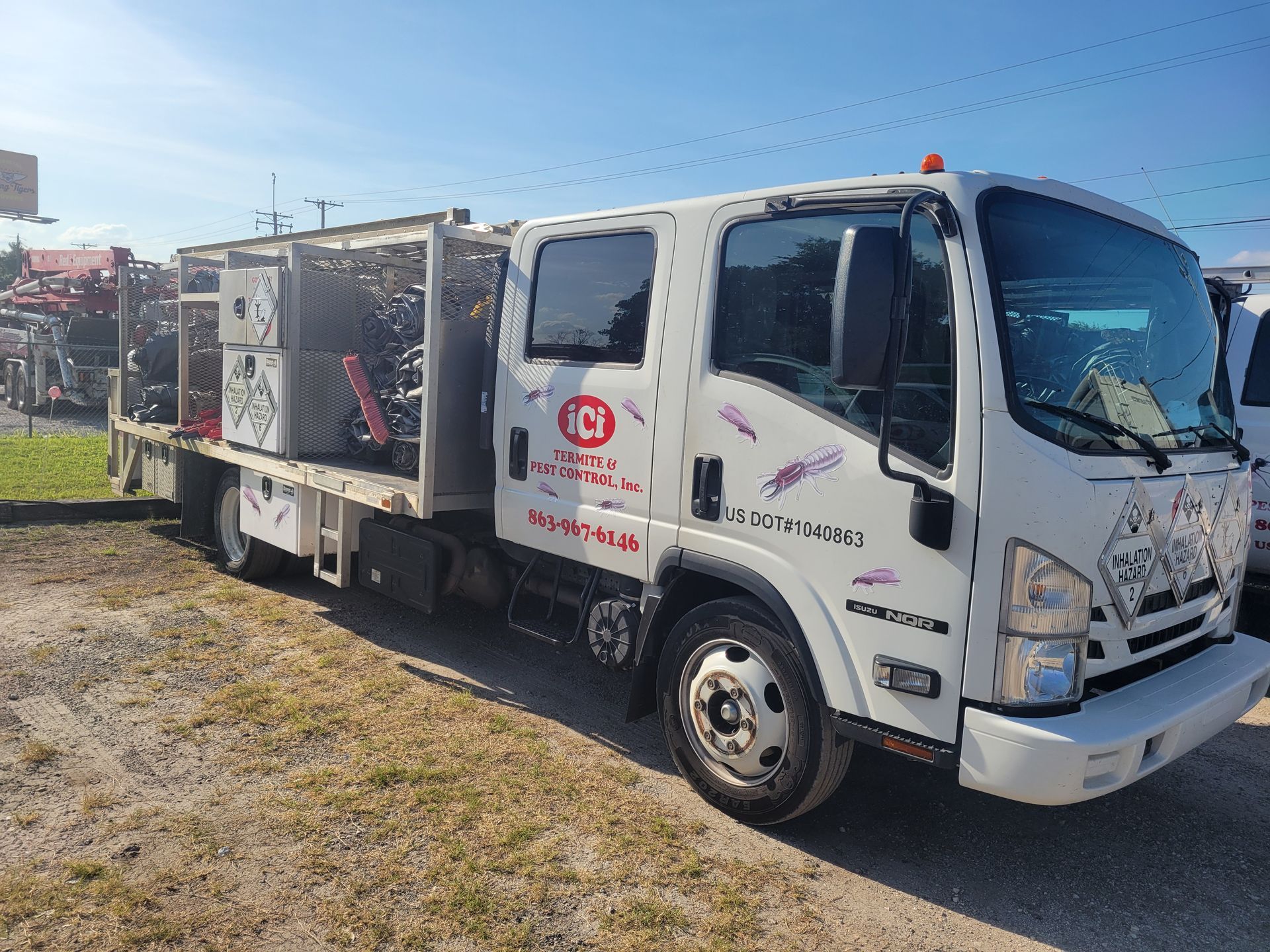 A white truck with a trailer attached to it is parked in a dirt lot.
