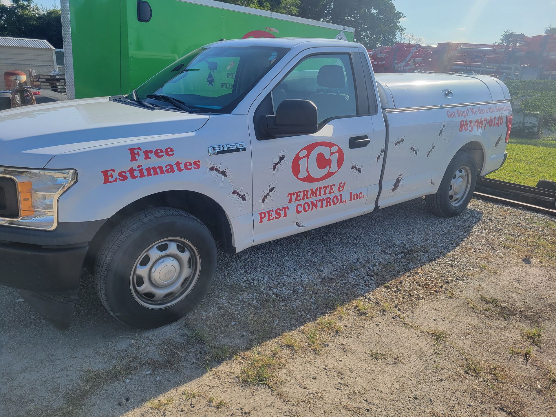 A white truck is parked on a gravel road next to a green truck.