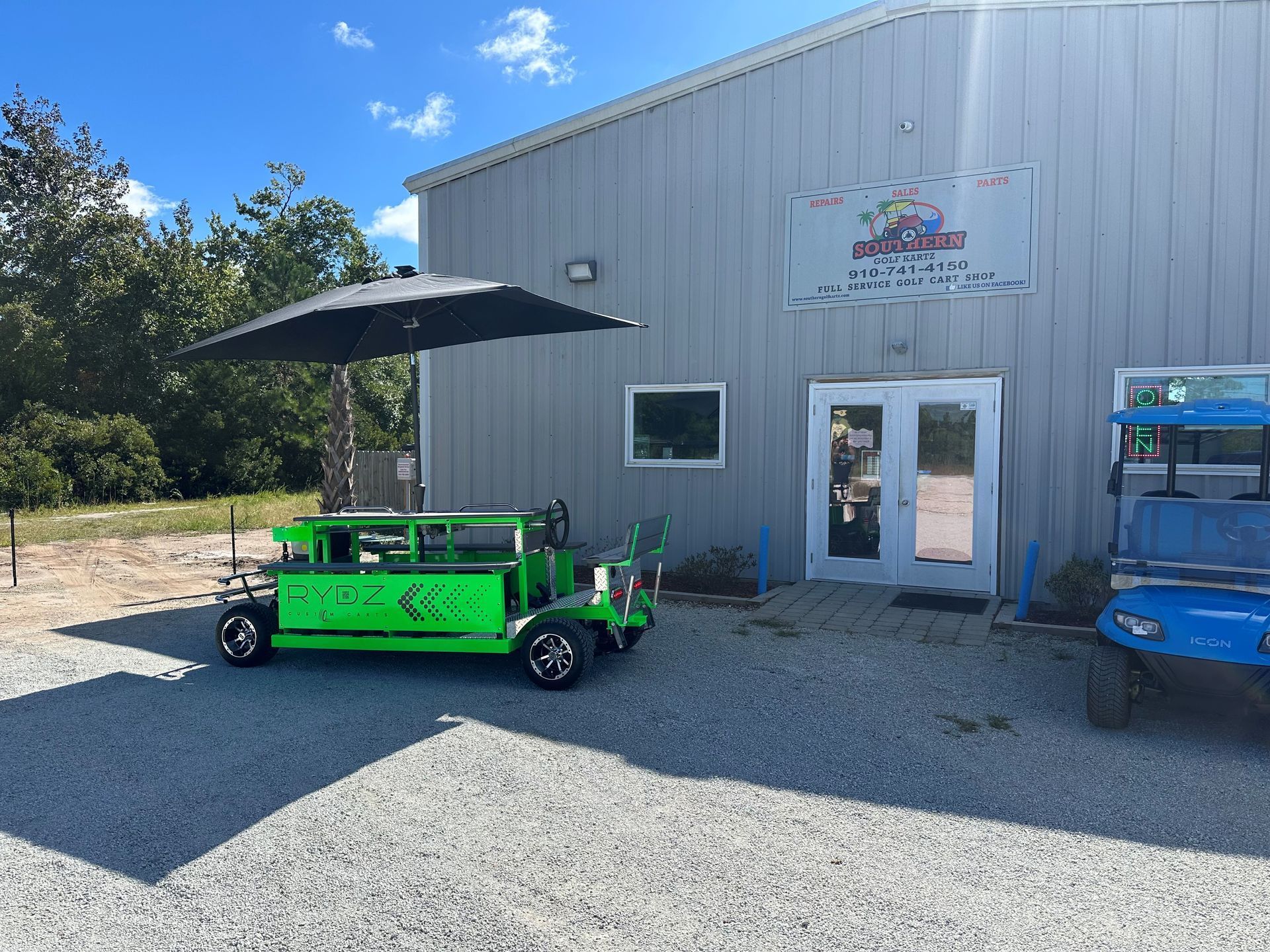 A green golf cart with an umbrella is parked in front of a building.